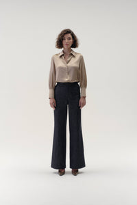 Woman wearing a beige blouse and dark pants on a white background