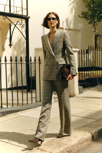 Woman in a plaid suit walking outdoors on a sunny day.